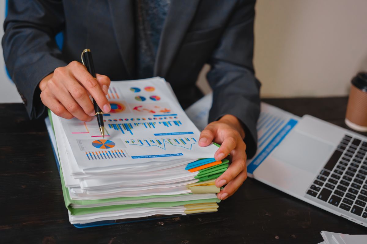 Ottawa Accounting Firm Helping Business Owners Save on Taxes Person reviewing a stack of printed financial reports with a pen, laptop open beside them