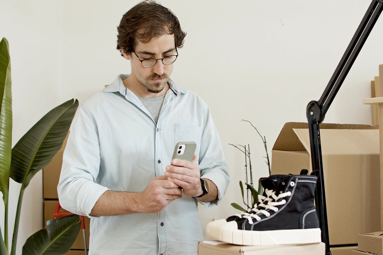 Retailer checking an order on his phone beside shipping boxes