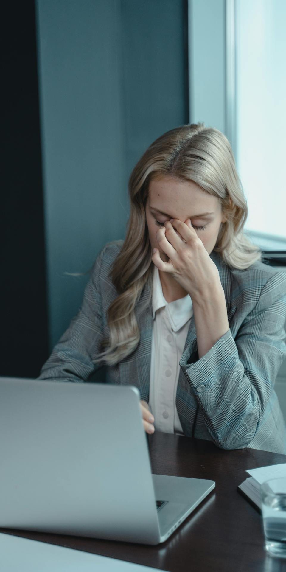 Woman at a laptop with her hand on her forehead, looking stressed